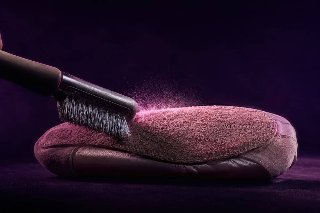 A steel-bristle brush drawn across the suede sole of an upturned slipper, lifting the fibres